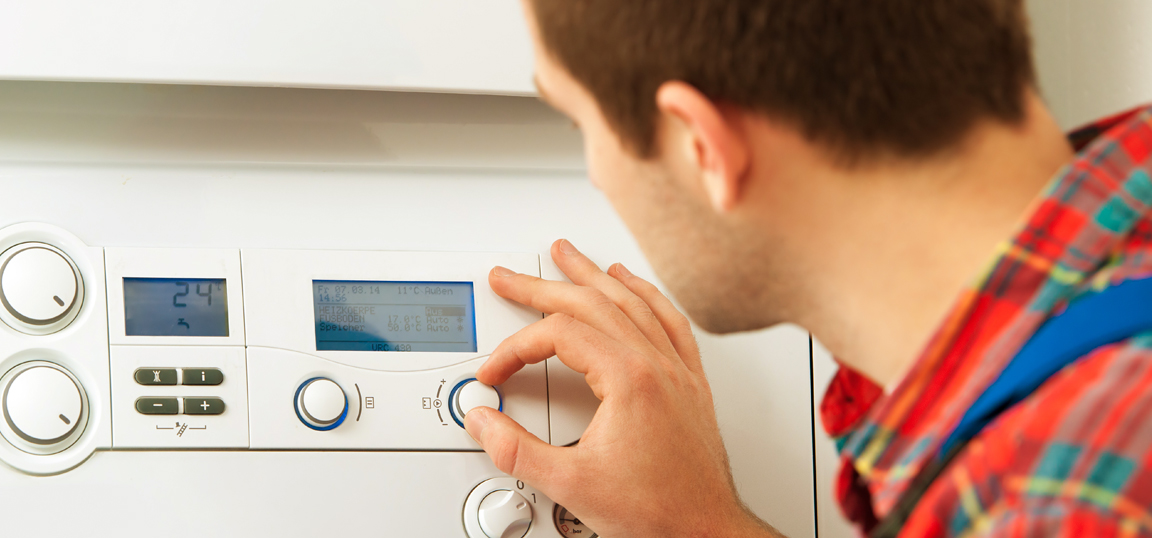 Man in red shirt near boiler, turning the temperature down on his heating system