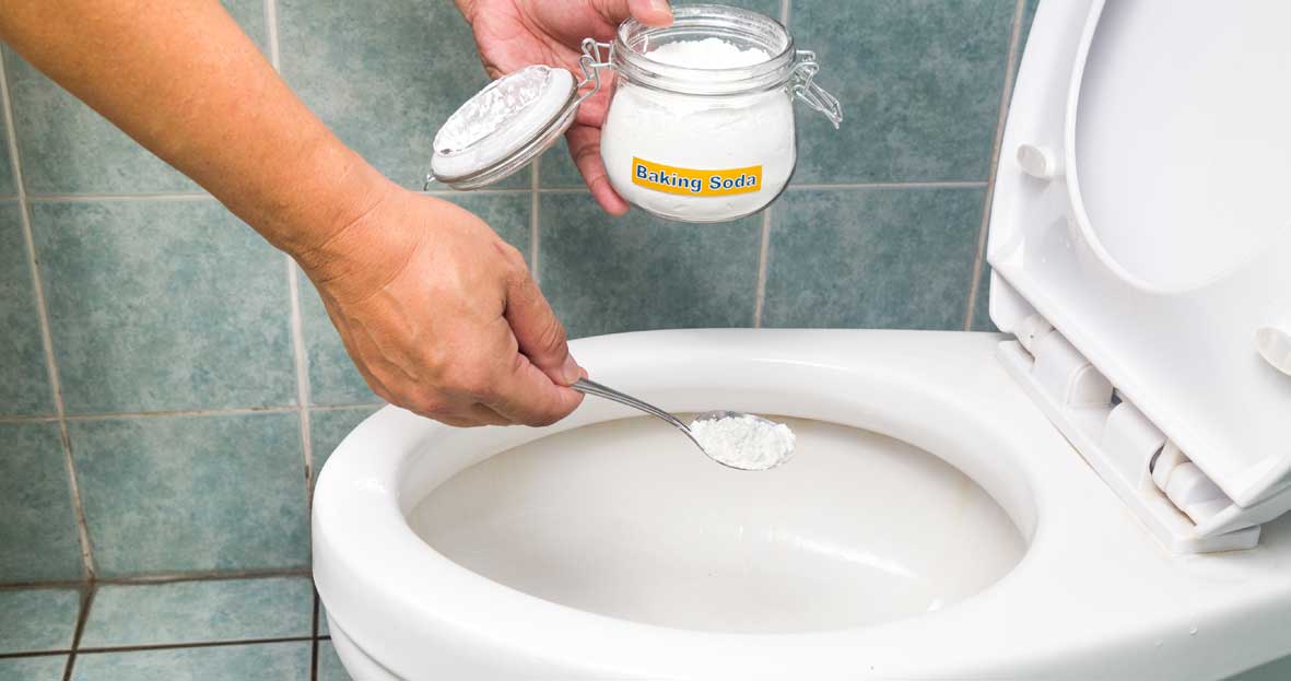 An image of a white toilet with the seat up. There is a glass jar labelled 'Baking soda', from which someone is pouring a spoonful into the toilet bowl.