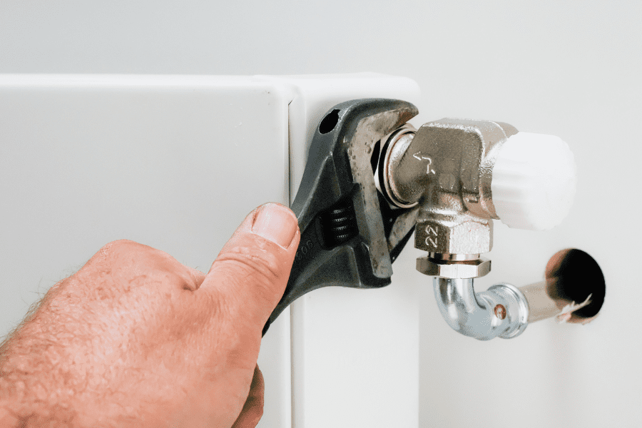 A person uses a metal spanner to tighten a radiator valve on a leaking radiator.