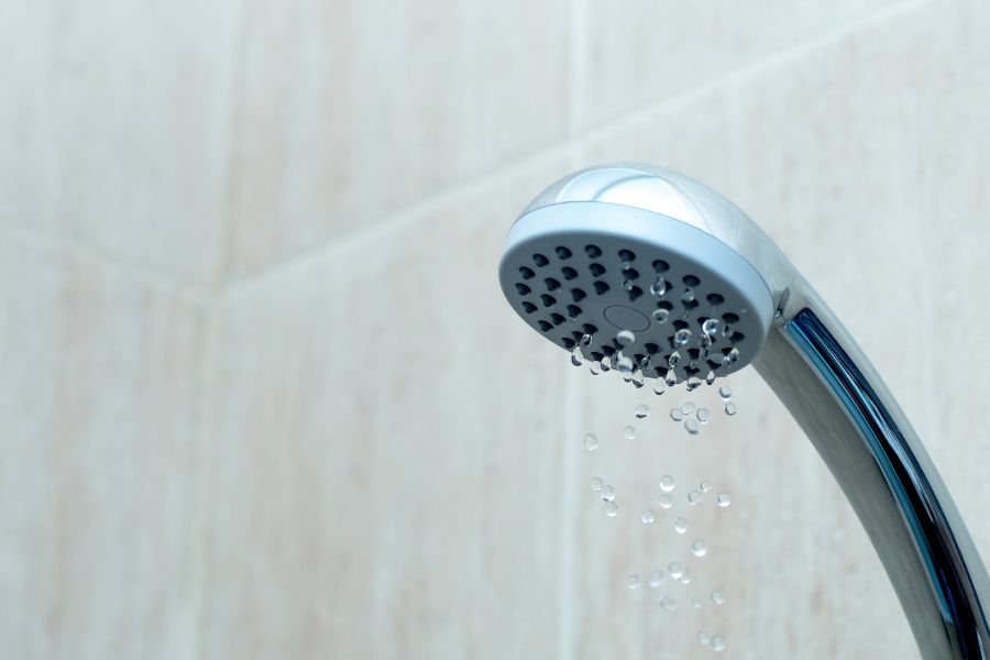 A close up of a showerhead, with water trickling out to show it has low water pressure.