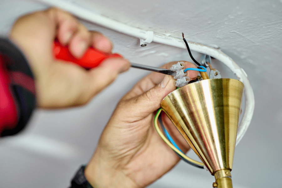 A person unscrewing the wiring connections of a terminal box to remove a light fitting.